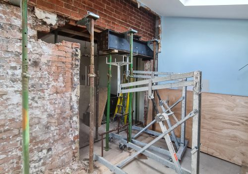 An opening in brickwork, with a large steel being lifted into place by a lifting device.