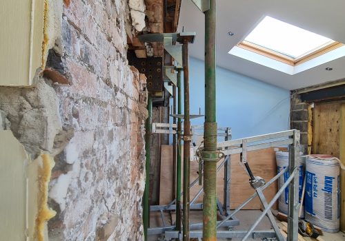 An opening in brickwork, with a large steel being lifted into place by a lifting device.