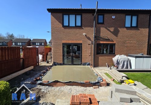 A view of where an extension will be built, there is a fresh concrete slab being poured.